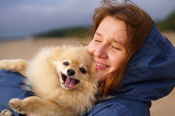 Happy young woman or teenager girl walking with her pet Pomeranian Spitz dog on the beach, hold...