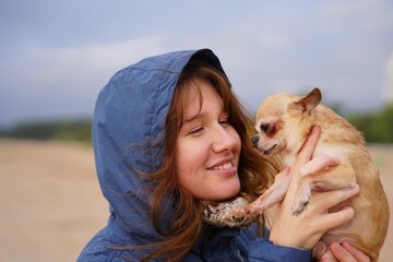 Happy young woman or teenager girl walking with her little pet Chihuahua or Toy terrier dog on the beach, hold puppy on hands. People love animals concept.