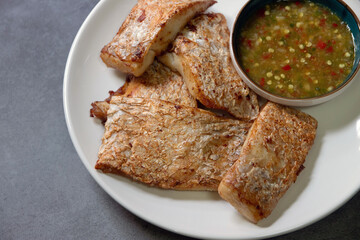 Deep fried sea bass with spicy sauce on white plate.