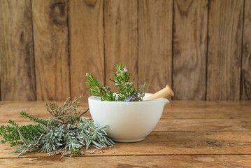 Medicinal plants concept; rosemary and thymus plants; white mortar and pestle on the rustic wooden...