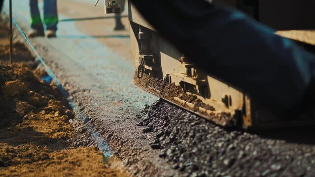 The process of road construction where fresh asphalt is laid over a gravel layer. A worker spreads asphalt and a special asphalt paver works.