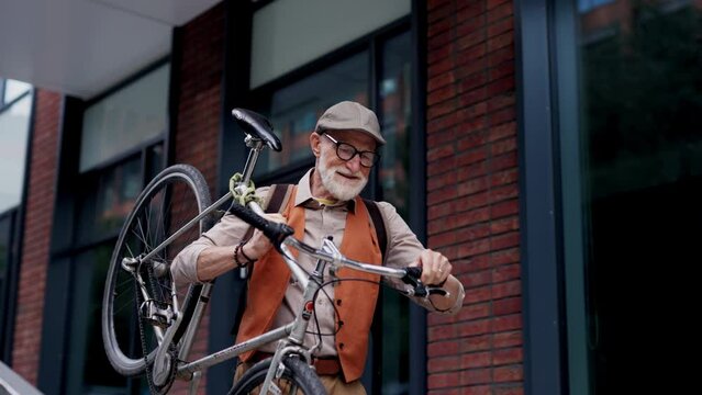 Elderly man, cyclist traveling through the city by bike, carrying bicycle on shoulder. Senior city commuter riding a bike.