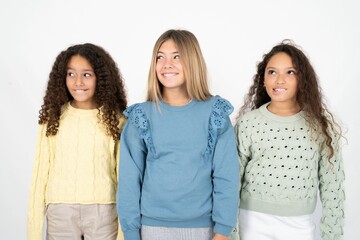 Amazed Three beautiful multiracial kid girls  bitting lip and looking tricky to empty space.