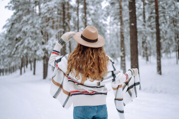 Fototapeta premium Beautiful woman posing with her back in the winter forest. Great winter weather and atmosphere. She is dressed in a winter coat, hat and scarf. Happy winter time. Christmas.
