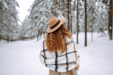 Fototapeta premium Beautiful woman posing with her back in the winter forest. Great winter weather and atmosphere. She is dressed in a winter coat, hat and scarf. Happy winter time. Christmas.
