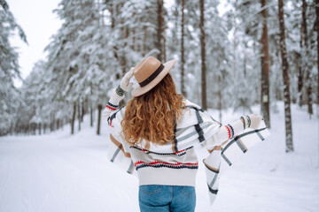 Beautiful woman posing with her back in the winter forest. Great winter weather and atmosphere. She is dressed in a winter coat, hat and scarf. Happy winter time. Christmas.