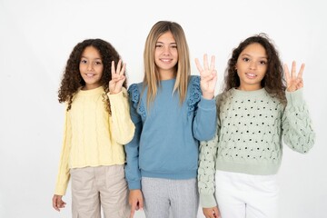 Fototapeta premium Three beautiful multiracial kid girls showing and pointing up with fingers number three while smiling confident and happy.
