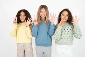 Fototapeta premium Three beautiful multiracial kid girls showing and pointing up with fingers number seven while smiling confident and happy.