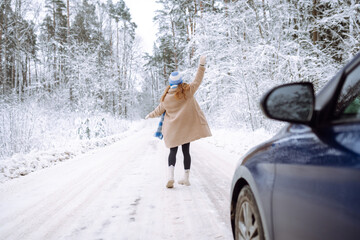 Beautiful young woman near a car in a snowy forest. First snow, great mood.  A traveler poses near a car in nature. Concept of car travel, vacation.