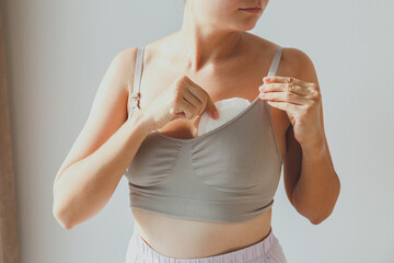 a young girl nursing mother uses disposable breast pads, puts them in her bra, her face is not visible. - obrazy, fototapety, plakaty