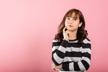 In a studio shot on a pink background, an Asian woman stands with her chin in her hand, showing a...