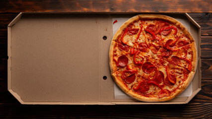 Pepperoni pizza with bell peppers in open carton box on dark wooden table flat lay with copy-space