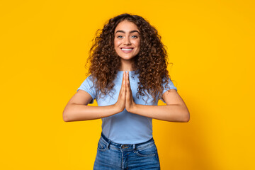 Grateful woman with hands in prayer pose on yellow background
