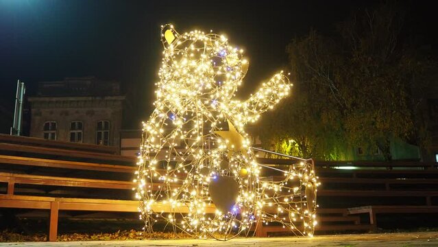 Small architectural form bear with raised paws, made of metal structures and garlands. Light bulbs glow in the shape of Teddy Bear or Winnie the Pooh. Christmas night decoration of streets and squares