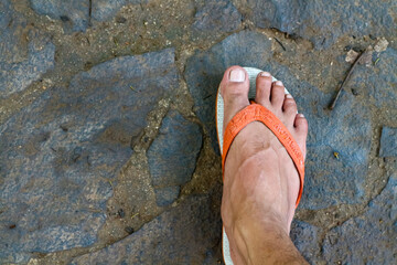 Men's feet with orange sandals on the background of a stone wall.