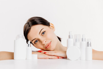 Cosmetics based on natural ingredients, scrub, tonic, body care. Production of natural cosmetics. A young woman on a light background among jars, bottles and tubes for cosmetic procedures.