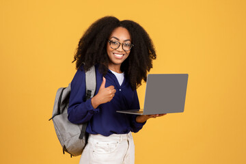 Cheerful student with laptop and backpack on yellow background