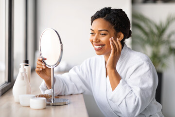 Beautiful Black Lady Looking In Mirror And Making Skincare Routine At Home