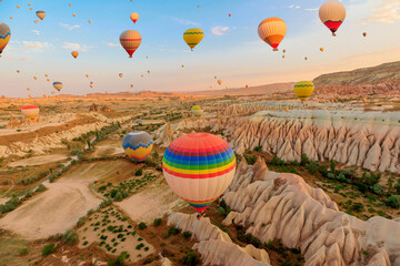 Cappadocia balloons in the sky. They capture first solar rays, casting an enchanting glow on the distinctive formations beneath them in Goreme Rose Valley, situated in Turkey's region of Cappadocia. - obrazy, fototapety, plakaty