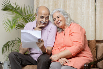 Happy indian senior couple looking in to the policy papers and smiling, After Retirement policy...