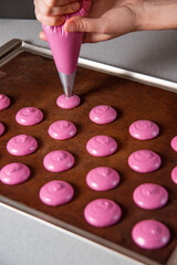 confectioner woman hands pipe macaroon butter from piping bag fitted onto parchment paper in circles