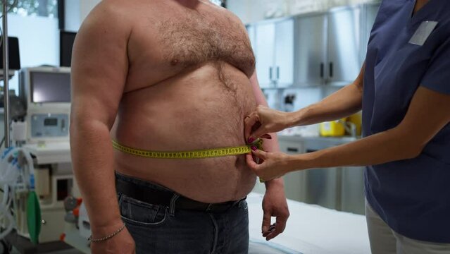Female doctor measuring waist of overweight patient using tape measure. Obesity affecting middle-aged men's health. Concept of health risks of overwight and obesity.