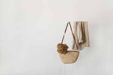 Elegant fashion accessory. Straw handbag with dried hydrangea flower, beige linen shirt blouse on...