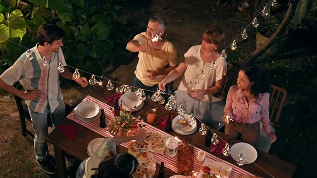 Top view. Family and friends gathering celebrating outdoor new year party and play festival sparklers together having enjoy at home. Big family multi-ethnic celebrating outdoors party at garden.