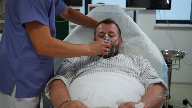 Nurse fitting oxygen mask on patient in hospital bed. Man in intensive care unit in hospital.