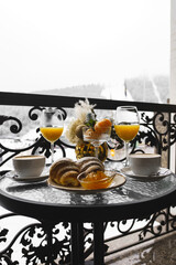 New Year's breakfast on the hotel balcony in the mountains. Coffee with croissant, juice and tangerines against the backdrop of snow-capped mountains. Concept of winter holidays