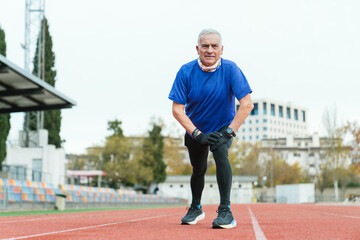 Fototapeta premium Elderly athletic man pauses for rest on track field, dressed in running attire, showing determination