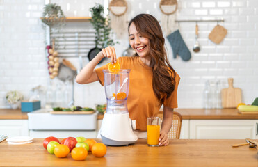 Portrait of beauty healthy asian woman making orange fruit smoothie with blender.girl preparing cooking detox cleanse with fresh orange juice in kitchen at home.health, vitamin c, diet, healthy drink.