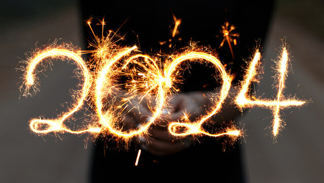 Girl holds a sparkler in her hands and draws 2024 with sparks. New Year 2024, creative idea.