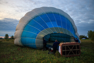 A group of men prepare a hot air balloon for flight using a gas burner and a fan.