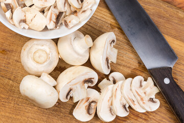 Partly sliced button mushrooms and kitchen knife on cutting board