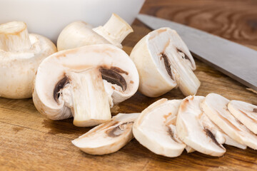 Whole, halved and sliced button mushrooms on cutting board closeup