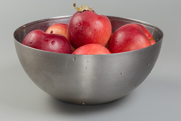 Washed red apples in metal bowl on a gray background