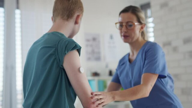 Nurse applying a continuous glucose monitor sensor on arm of a diabetic teenager. CGM device making life of teenage boy easier, helping manage his illness and focus on other activities.