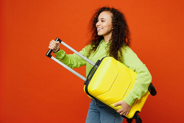 Side view traveler woman wears green casual clothes hold suitcase bag isolated on plain orange red...