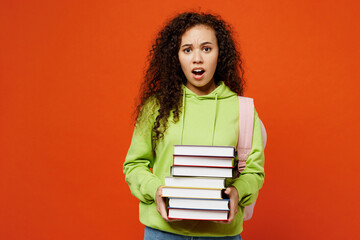 Young scared sad teen girl student of African American ethnicity wear casual clothes backpack bag hold stack of books isolated on plain orange red background. High school university college concept.