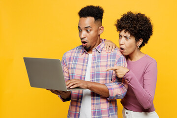 Shocked sad scared young couple two friends family IT man woman wearing purple casual clothes together hold use work on laptop pc computer surfing internet isolated on plain yellow orange background. - obrazy, fototapety, plakaty
