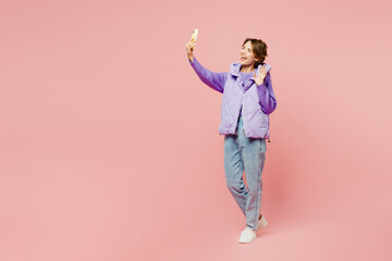 Full body young woman wear purple vest sweatshirt casual clothes doing selfie shot on mobile cell phone post photo on social network isolated on plain pastel light pink background. Lifestyle concept.