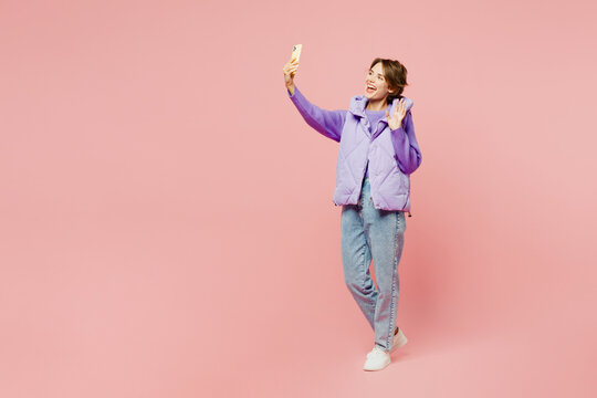 Full body young woman wear purple vest sweatshirt casual clothes doing selfie shot on mobile cell phone post photo on social network isolated on plain pastel light pink background. Lifestyle concept.