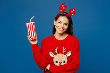 Merry cool young Latin woman in red Christmas sweater decorative fun deer horns on head posing hold...