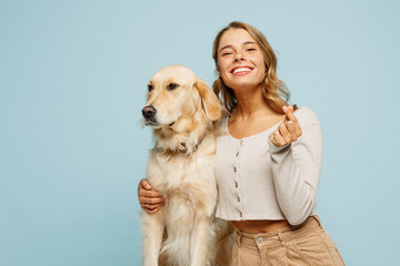 Young owner woman with her best friend retriever dog wear casual clothes show love hand gesture with crossed fingers isolated on plain pastel light blue background studio. Take care about pet concept.