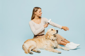 Full body happy young owner woman wear casual clothes cleaning shirt fur with roller sits near her best friend retriever dog isolated on plain light blue background studio Take care about pet concept