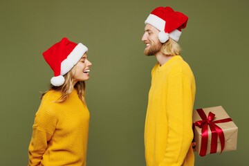 Side view merry young couple two friend man woman wear sweater Santa hat posing give present box...