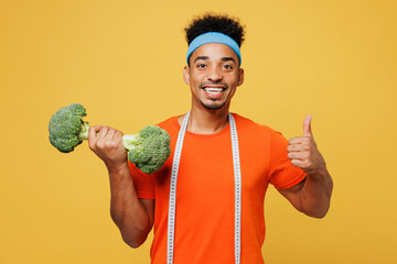 Young fitness trainer instructor sporty man sportsman wear orange t-shirt hold dumbbell broccoli measure tape spend time in home gym isolated on plain yellow background. Workout sport fit abs concept. - Powered by Adobe