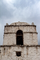 White Bell tower of a Christian church in a village around Sangalle, Canyon de Colca, Peru. Andes mountains in the background with fog.