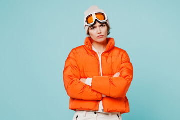Skier frowning young woman wears warm padded windbreaker jacket hat ski goggles mask hold hands crossed folded travel rest spend weekend winter season in mountains isolated on plain blue background.